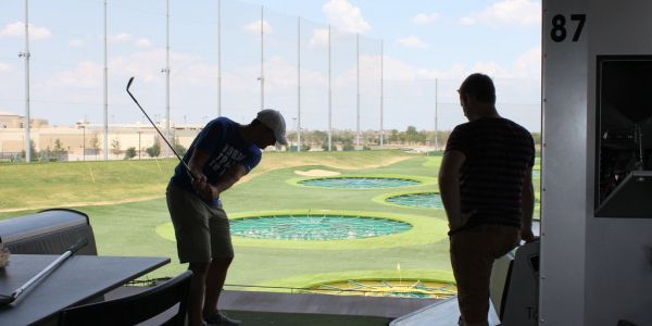 The Arbors at Wolf Pen Creek apartments Two people at a golf driving range, one is swinging a club, the other watching. Sunny day with scattered clouds.