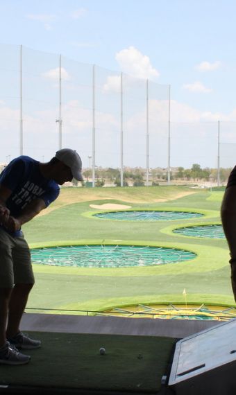 The Arbors at Wolf Pen Creek apartments Two people at a golf driving range, one is swinging a club, the other watching. Sunny day with scattered clouds.