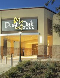 The Arbors at Wolf Pen Creek apartments Entrance of Post Oak Mall at dusk, with lit signage and surrounding plants.