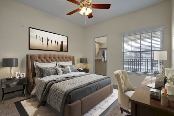The Arbors at Wolf Pen Creek apartments A cozy bedroom with a large bed, desk, ceiling fan, and walk-in closet.