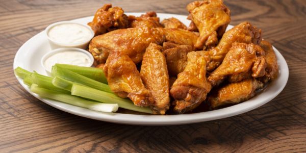 A plate of buffalo chicken wings with celery sticks and dipping sauce on a wooden table near The Arbors at Wolf Pen Creek Apartments.