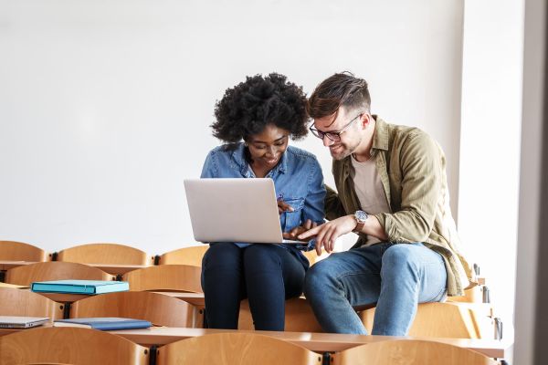 Two people sitting in a lecture hall, sharing a laptop and smiling near The Arbors at Wolf Pen Creek apartments.
