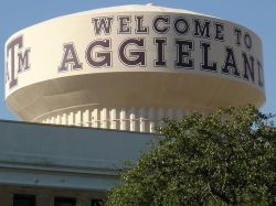The Arbors at Wolf Pen Creek apartments Water tower with "WELCOME TO AGGIELAND" and Texas A&M logo, partially obscured by greenery.