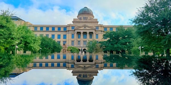 An elegant, dome-topped building with trees reflecting in a pool on a sunny day near The Arbors at Wolf Pen Creek apartments.